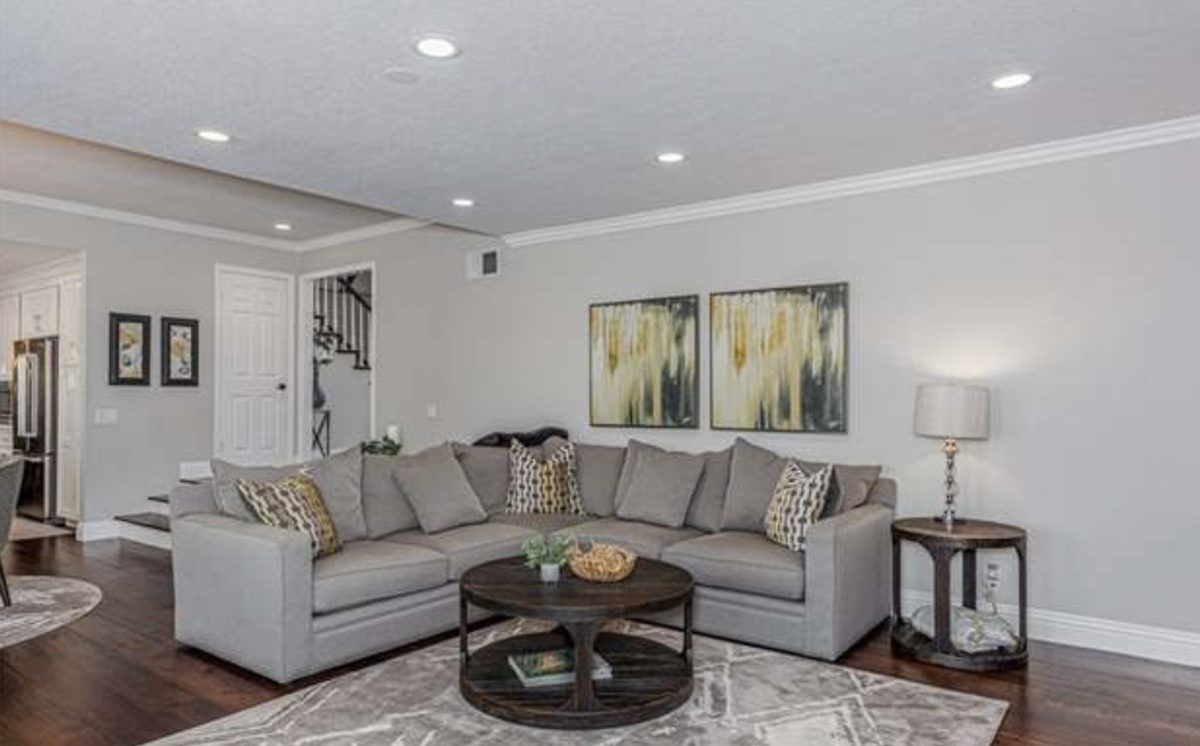 Light grey sectional sofa under two gold and black abstract canvases, round walnut coffee table on a pale grey rug, crystal table lamp on a round side table